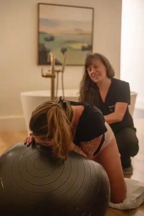Hannah laboring on a birth ball while her midwife offers support